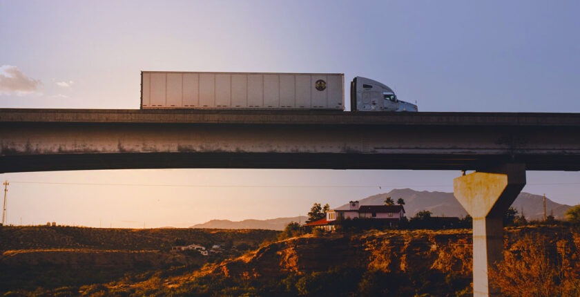 Tractor trailer driving across bridge at sunrise in Southern California hills