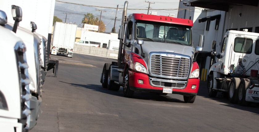 Red tractor trailer can driving through truck company parking lot