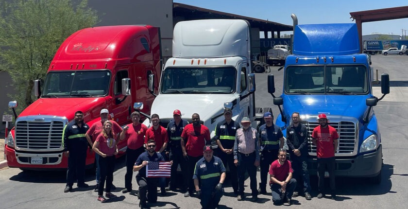 Group of Veteran TCI employees attending in front of red, white, and blue trucks, holding an American flag.