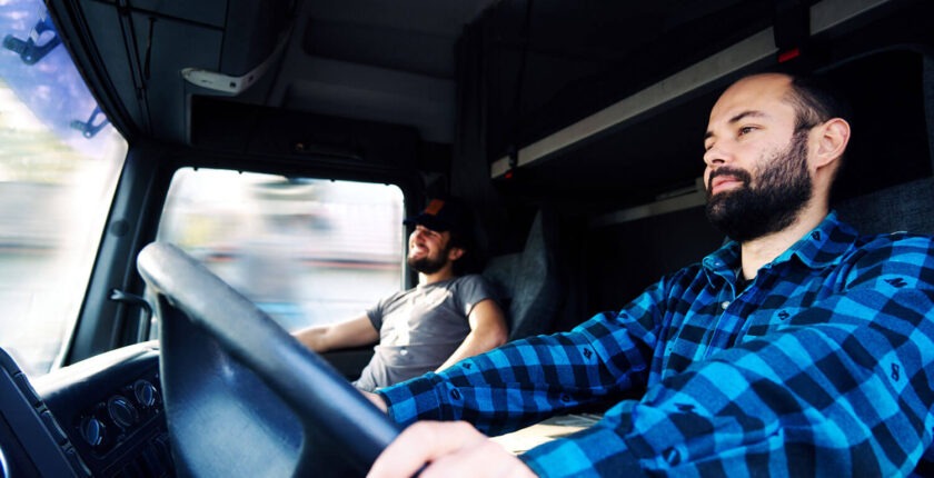 Two men in can of semi truck driving down highway.