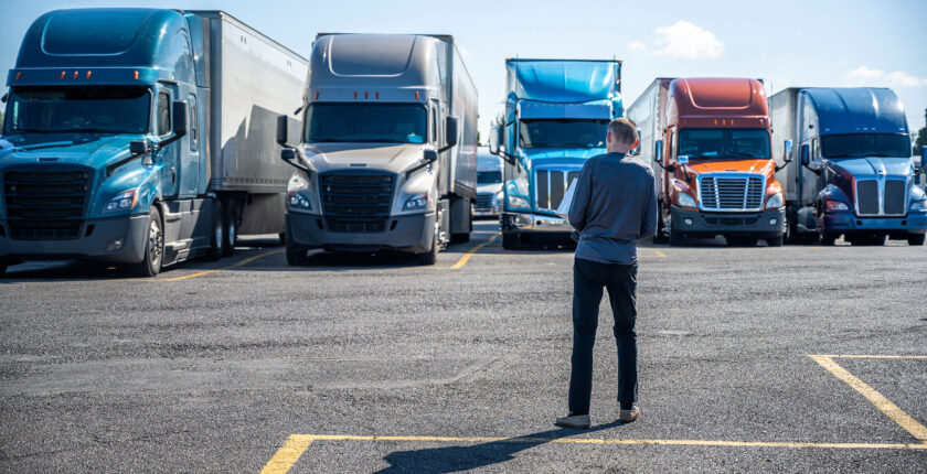 Truck driver standing in parking lot in front of row of semi-tractors