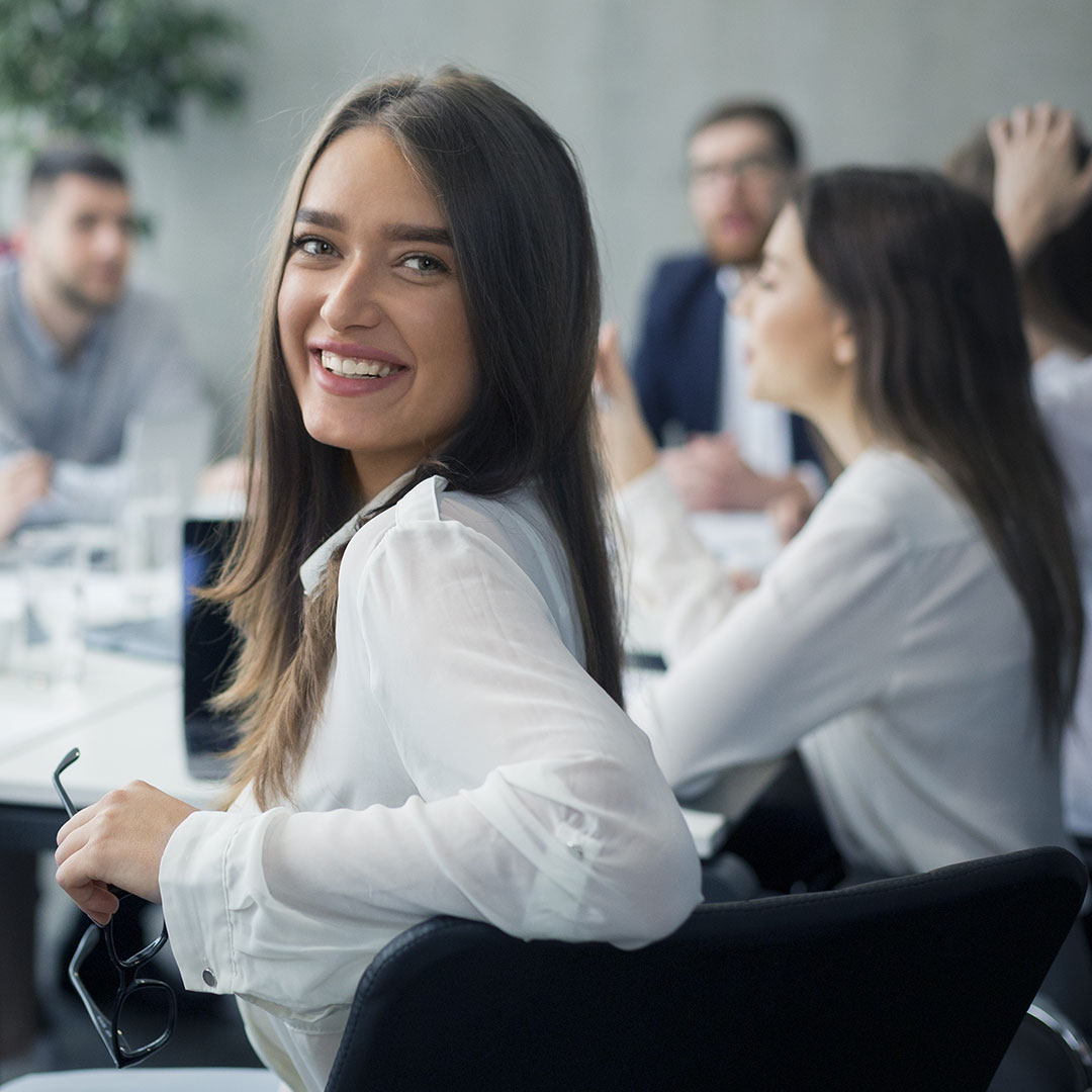 Woman at meeting table, turning around and smiling at camera