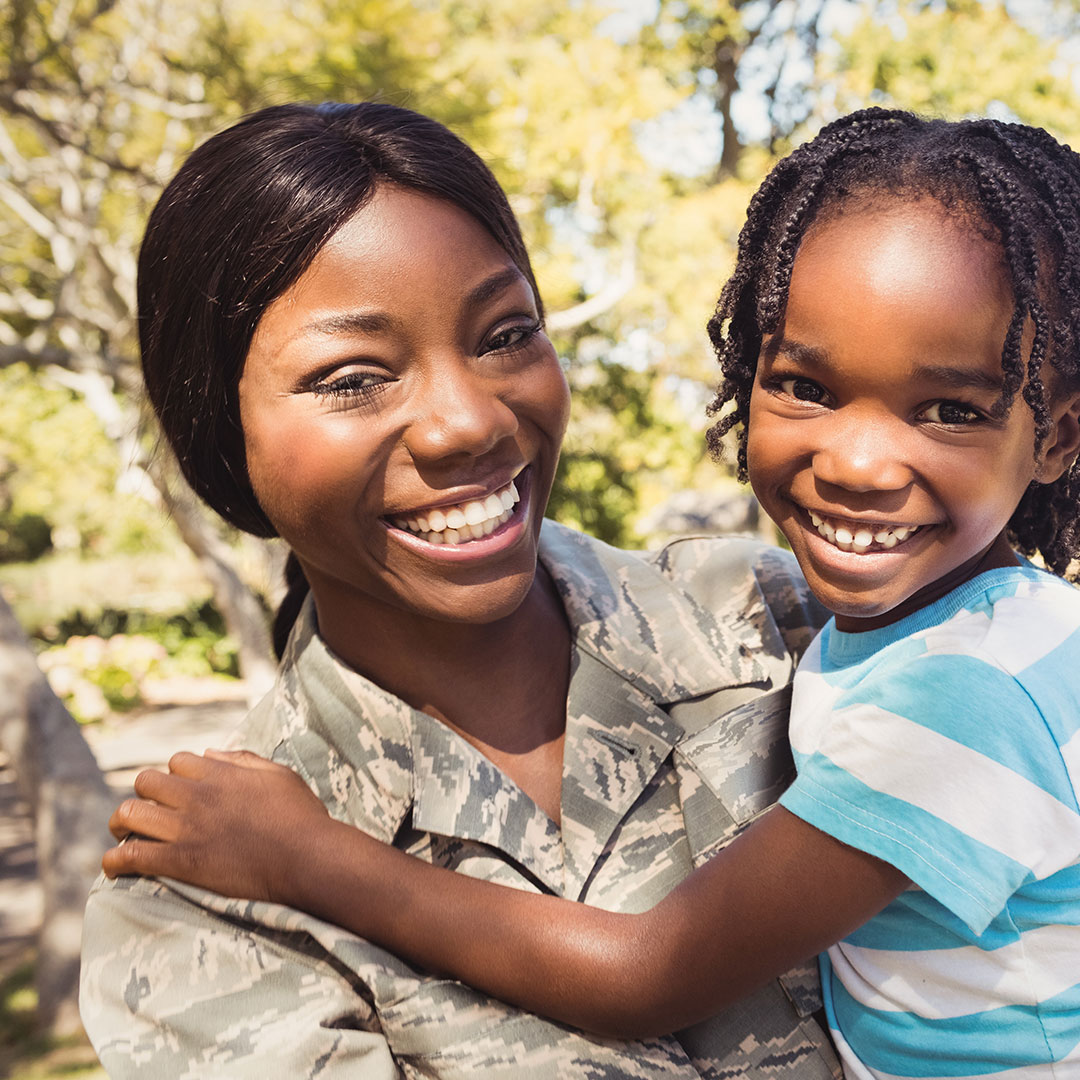 Military mom in fatigues holding young daughter in her arms