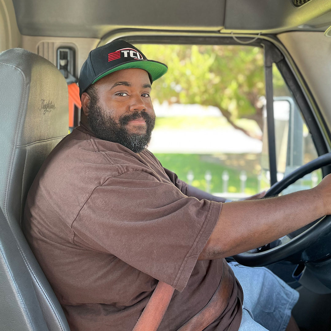 TCI driver at the wheel in the cab, wearing a TCI baseball cap